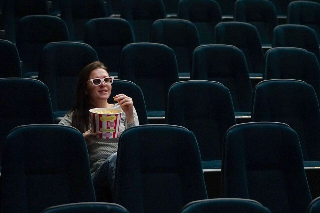 Une femme profitant de son temps au cinéma, tenant une barquette de pop-corn et arborant une expression joyeuse, totalement immergée dans l'expérience cinématographique.